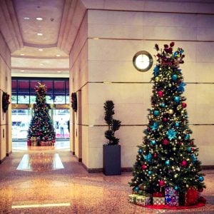 Two large, brightly decorated Christmas trees in a lobby with marble floors