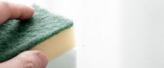 A hand holding a yellow and green sponge, wiping down a white fiberglass planter surface