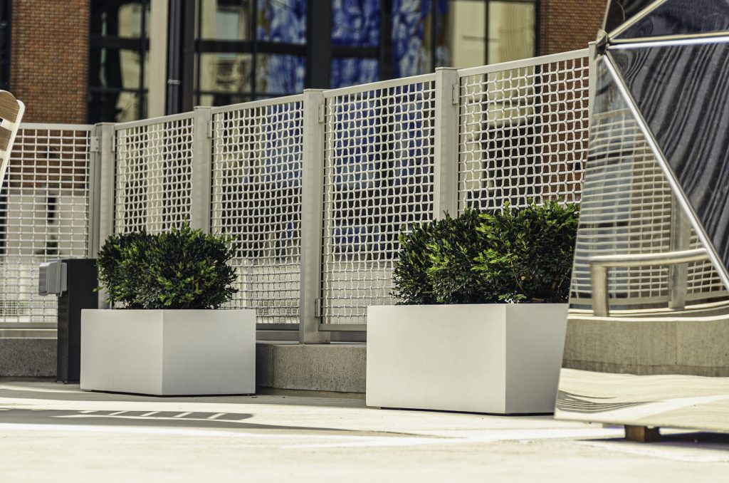 two rectangular commercial planters outside with bushes planted in them