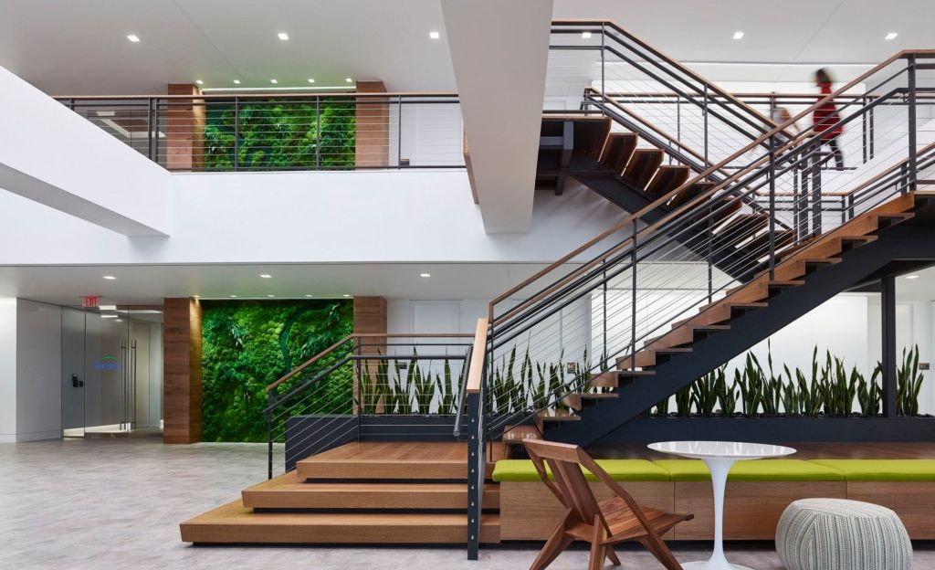 forest city office building entryway with metal and wood stairs, a plant wall, and a small table