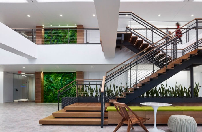 forest city office building entryway with metal and wood stairs, a plant wall, and a small table