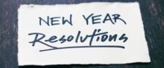A handwritten note reading “New Year Resolutions” on a small piece of white paper placed on a dark wooden surface