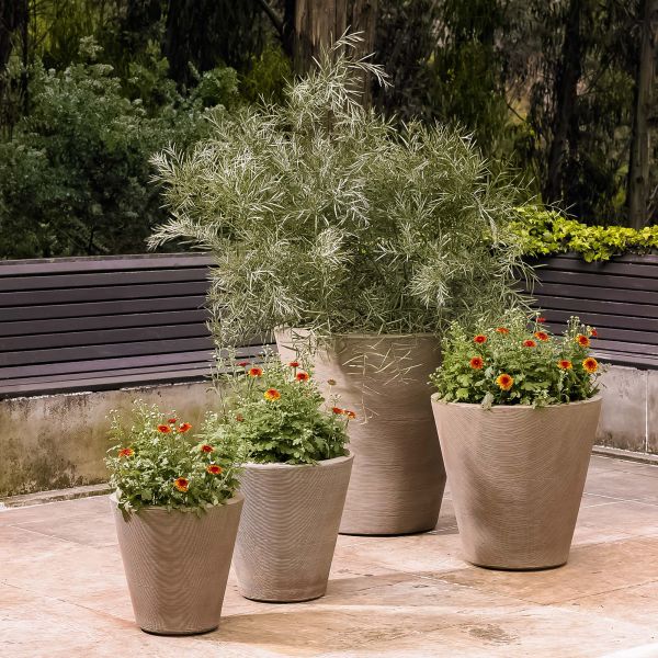 A group of round brown outdoor planters in varying sizes, filled with flowering plants and foliage, arranged on a patio