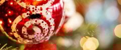 A red Christmas bauble decorated with white and glittery swirl patterns, hanging from a decorated fir tree branch