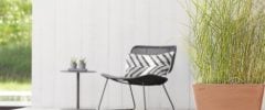 An outdoor patio featuring a square terracotta-colored eco-friendly planter with tall grasses near a black chair