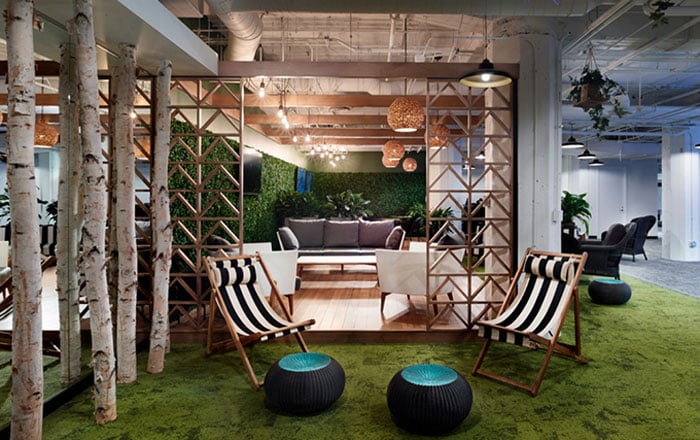 interior office with tree trunk columns, plant wall, grassy green carpet, and striped folding chairs as an example of biophilic design in the workplace