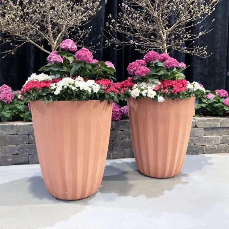 Tall tapered, ribbed planters finished in black sit on a stone patio outside the entrance of a modern office building.